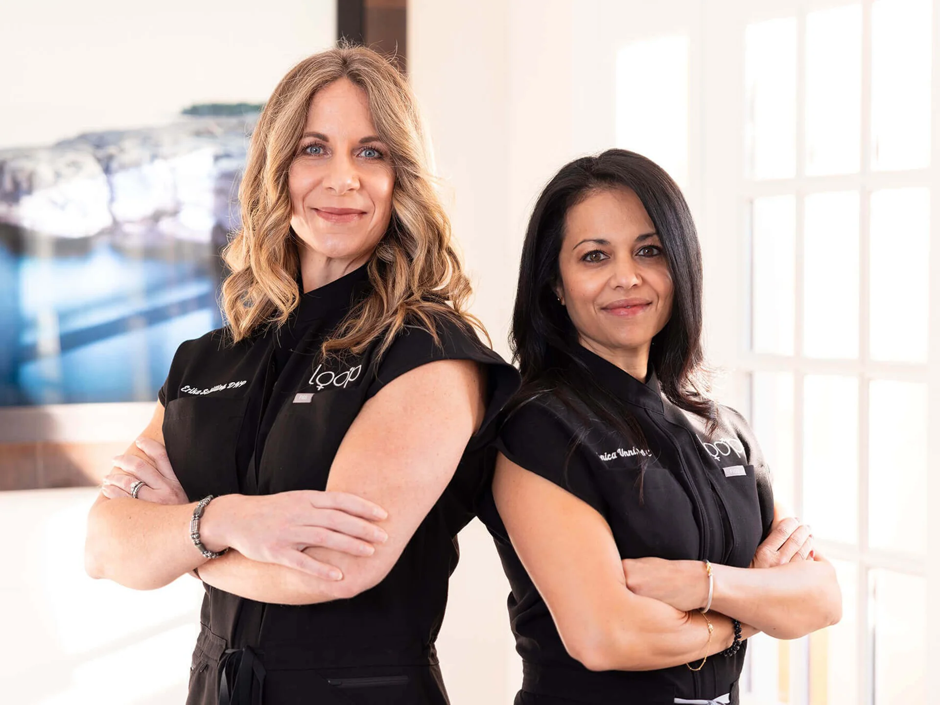 Two Loop Wellness Clinic providers in black Loop uniforms standing back to back with arms crossed