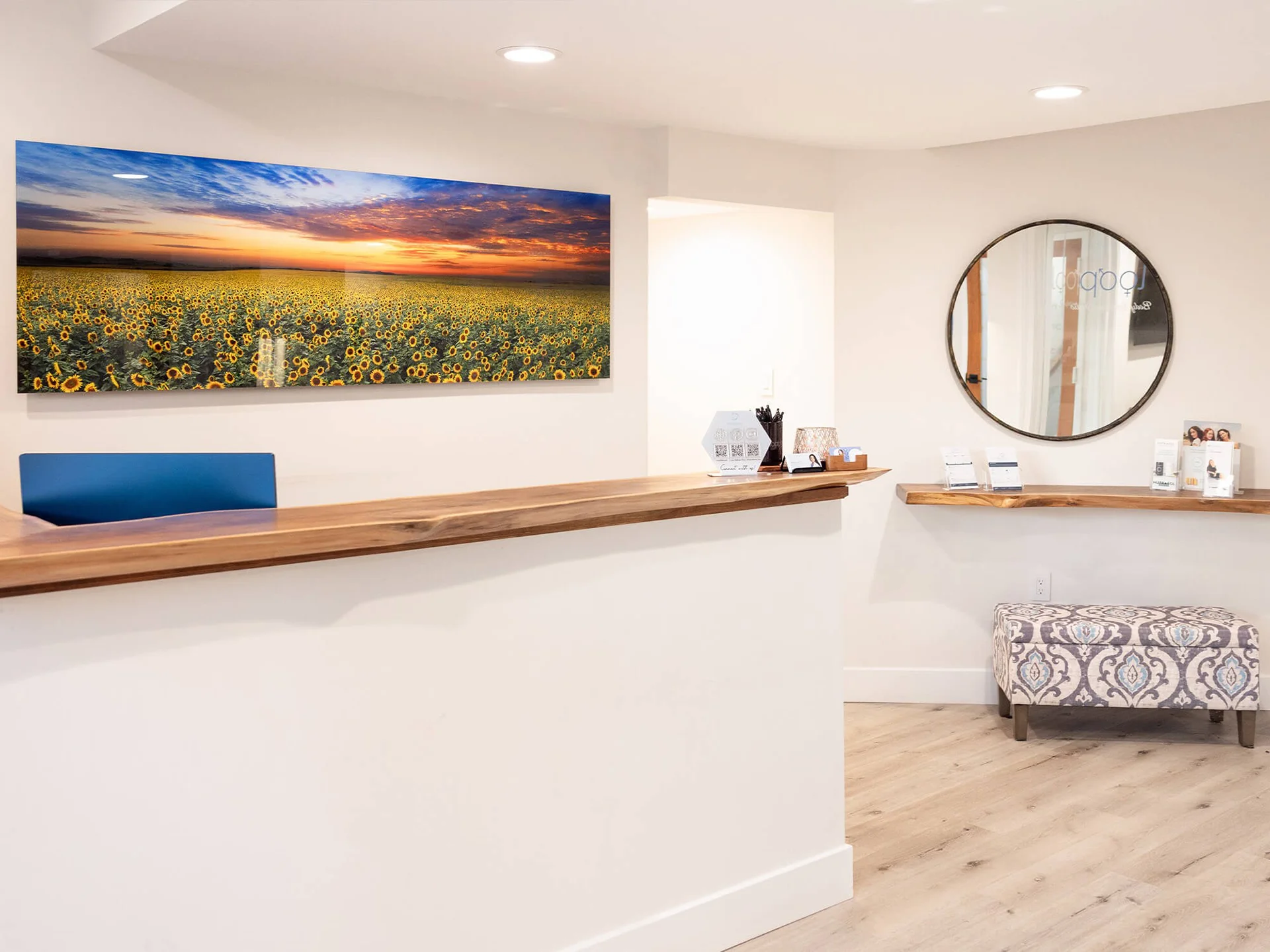 Bright Loop Wellness Clinic reception desk with a sunflower-field canvas and a round mirror